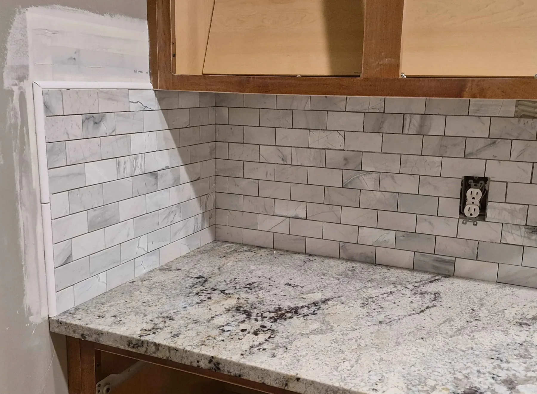 Marble-look subway tile backsplash above a granite countertop, mid-installation