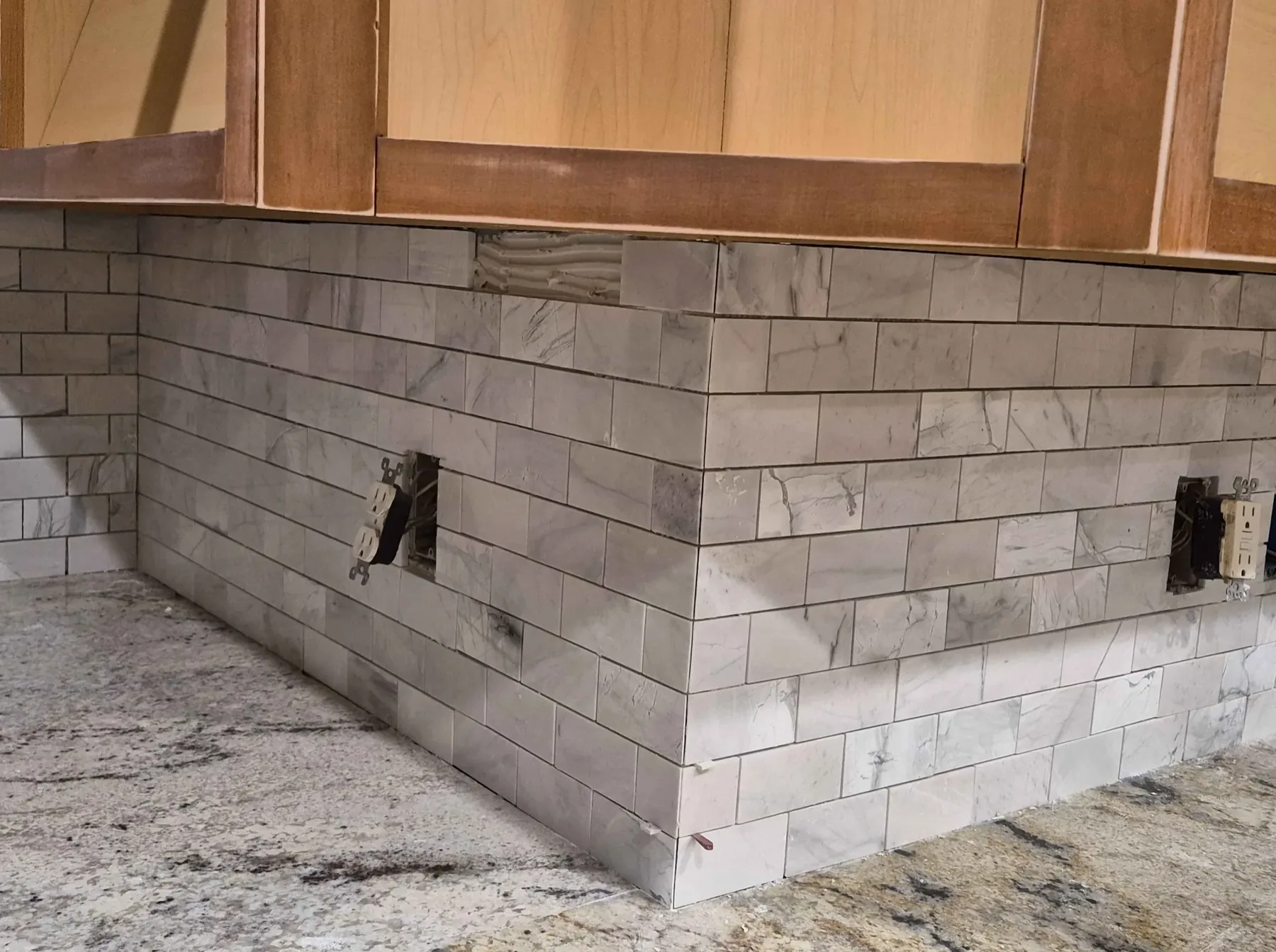 Marble-look subway tile backsplash wrapping a granite counter, mid-installation