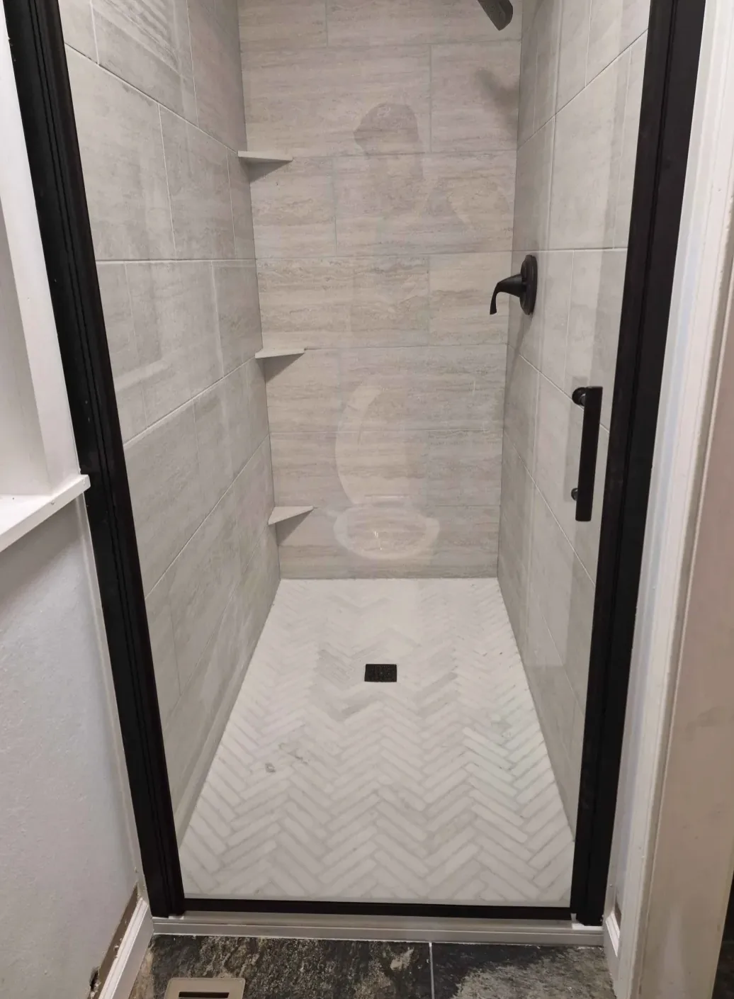 Shower with large wall tile, a herringbone floor and a black-framed glass door